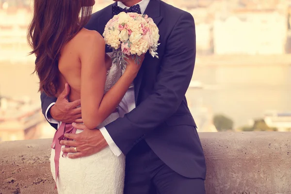 Detalhe de uma noiva e noivo abraçando. Noiva segurando lindo buquê de casamento — Fotografia de Stock