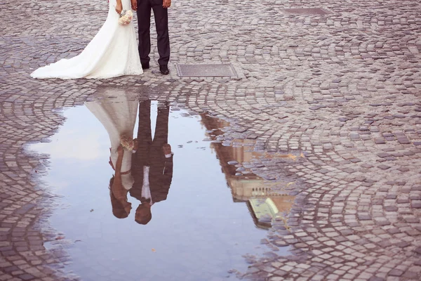 Bride and groom reflected in slop on paved road — Stock Photo, Image