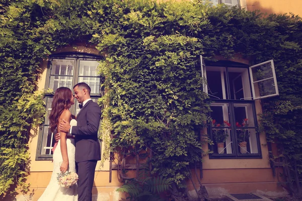 Sposa e sposo che si abbracciano di fronte a una bella casa ricoperta di edera — Foto Stock