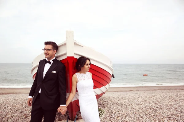 Bride and groom near big, red boat at the ocean — Stock Photo, Image