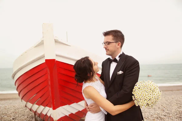 Bride and groom near big, red boat at the ocean — Stock Photo, Image