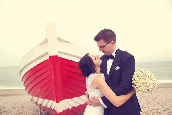 Bride and groom near big, red boat at the ocean — Stock Photo, Image