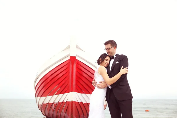 Bride and groom near big, red boat at the ocean — Stock Photo, Image