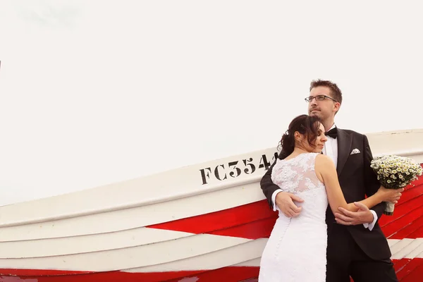 Bride and groom near big, red boat at the ocean — Stock Photo, Image