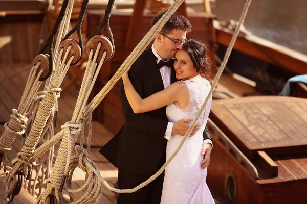 Bride and groom embracing near big ship with strings — Stock Photo, Image