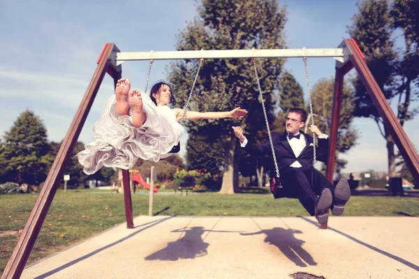 Bride and groom playing on a swing set — Stock Photo, Image