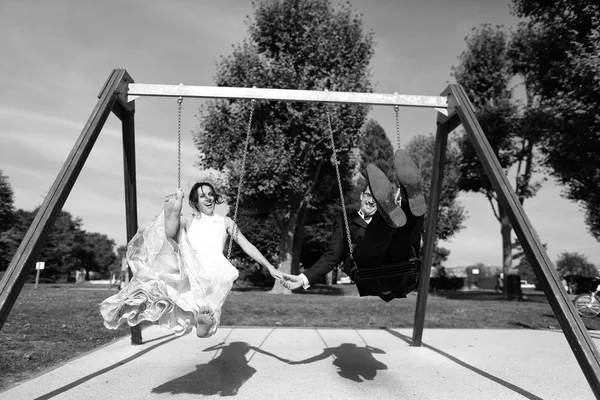 Bride and groom playing on a swing set — Stock Photo, Image