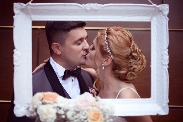 Noiva e noivo beijando através da moldura — Fotografia de Stock