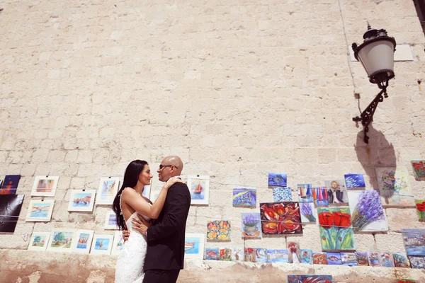 Bride and groom against a wall full of paintings — Stock Photo, Image