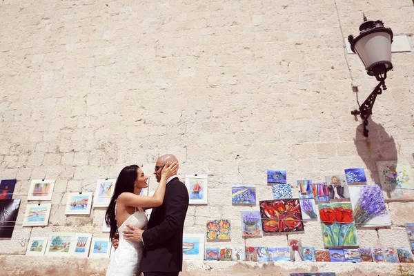 Bride and groom against a wall full of paintings — Stock Photo, Image