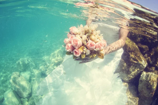 Mains d'une mariée tenant un bouquet de mariage sous l'eau — Photo