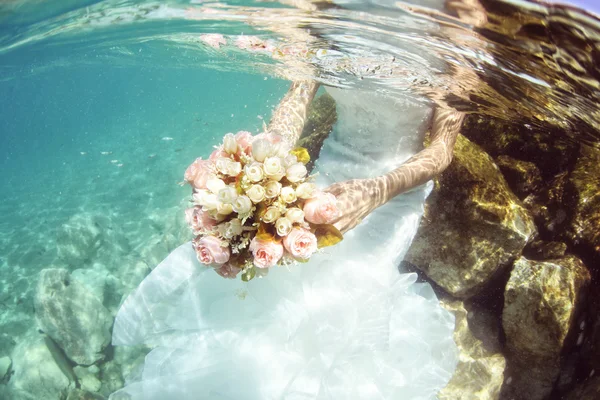 Mãos de uma noiva que mantém o buquê de casamento subaquático — Fotografia de Stock