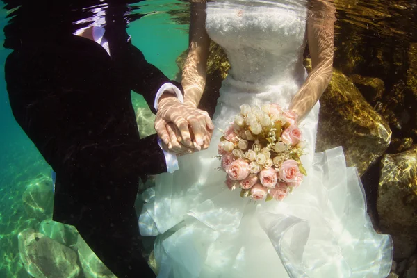 Bride and groom holding hands underwater — Stock Photo, Image