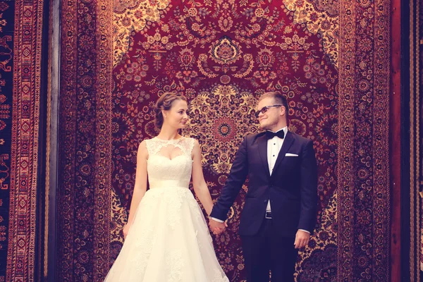 Bride and groom against a hanging carpet — Stock Photo, Image