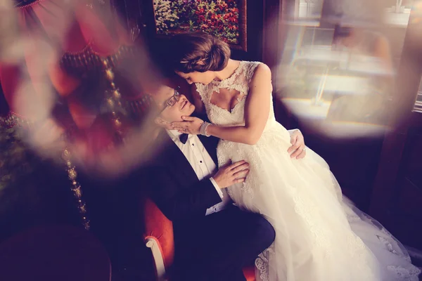 Bride and groom sitting on chair in a beautiful room — Stock Photo, Image