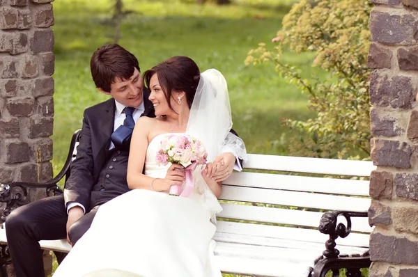 Bride and groom sitting on bench Stock Picture