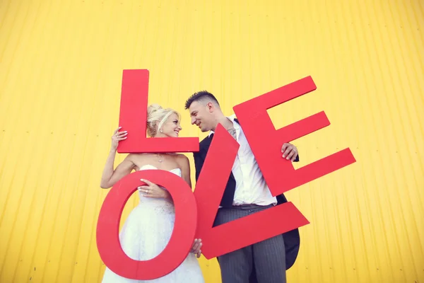 Bride and groom holding big LOVE letters — Stock Photo, Image