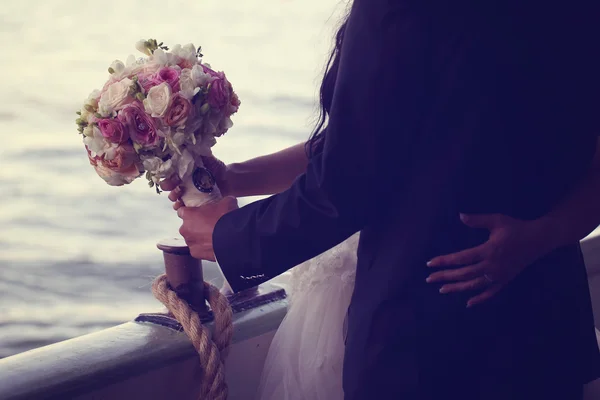 Hands of a bride holding wedding bouquet with her groom on boat — Stock Photo, Image