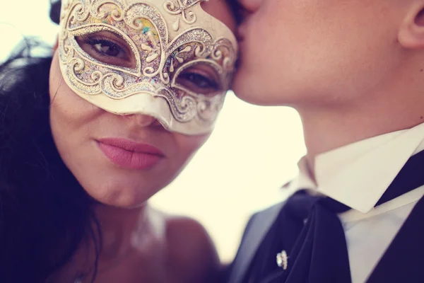 Bräutigam küsst seine Braut. Braut mit venezianischer Maske — Stockfoto