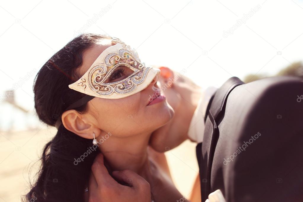Groom kissing his bride. Bride wearing venetian mask
