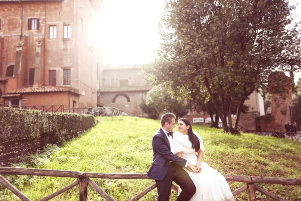 Bride and groom on wood fence near castle — Stock Photo, Image