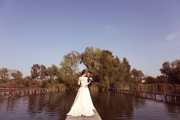 Bridal couple on wooden bridge at lake — Stock Photo, Image