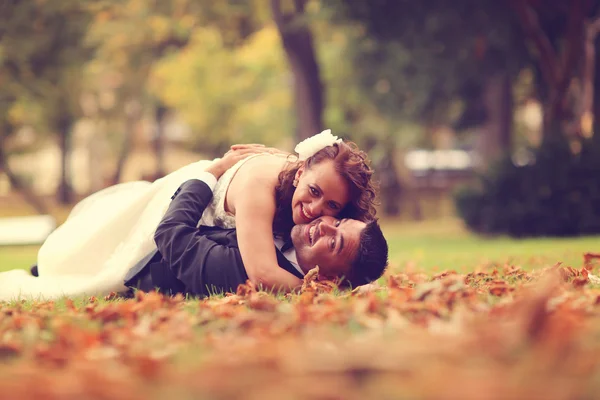 Bride and groom laying on autumn leaves — Stock Photo, Image