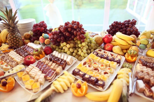 Tavola piena di frutta e piccole torte — Foto Stock