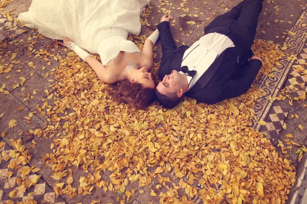 Bride and groom laying on autumn leaves — Stock Photo, Image