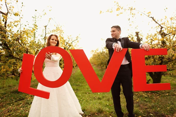 Bride and groom holding big LOVE letters — Stock Photo, Image