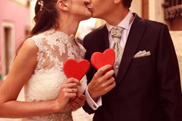 Bride and groom holding red hearts — Stock Photo, Image