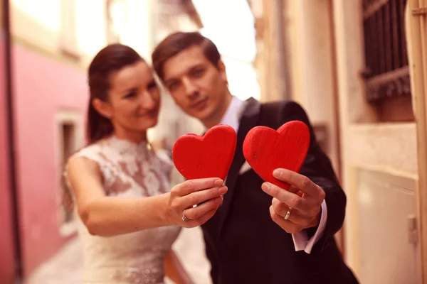 Bride and groom holding red hearts — Stock Photo, Image