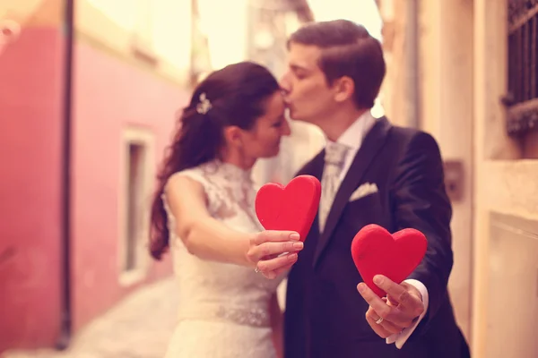 Bruden och brudgummen håller röda hjärtan — Stockfoto