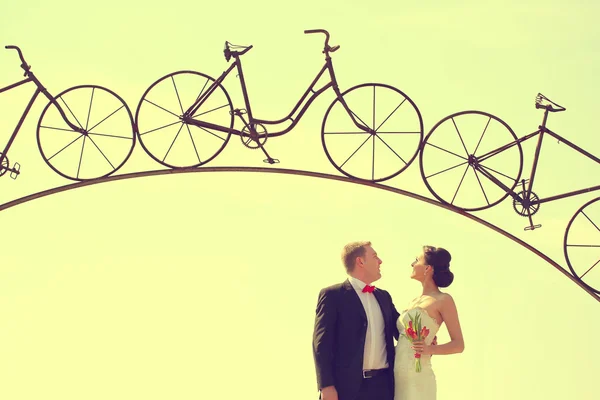 Bride and groom under a iron arch in a bicycle form — Stock Photo, Image