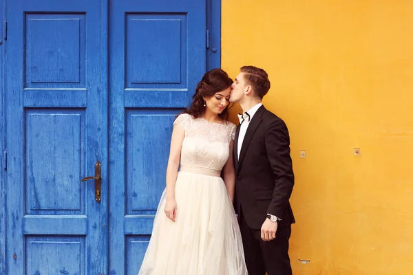 Noiva e noivo contra parede amarela e porta azul — Fotografia de Stock