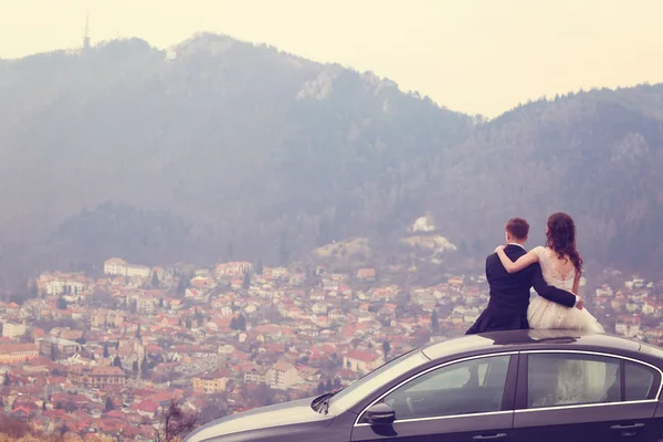 Bride and groom sitting on their car — Stock Photo, Image