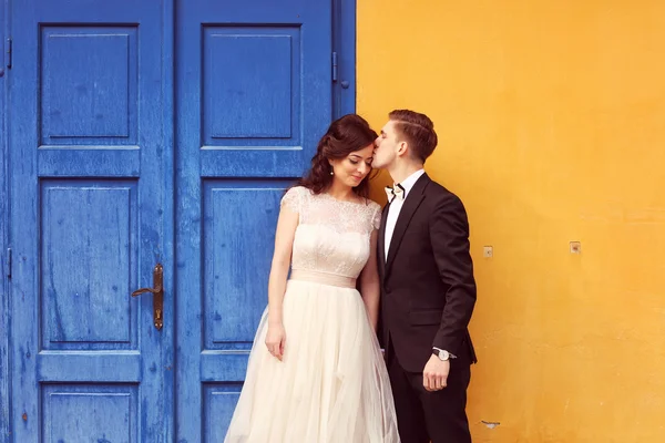 Bride and groom against yellow wall and blue door — Stock Photo, Image