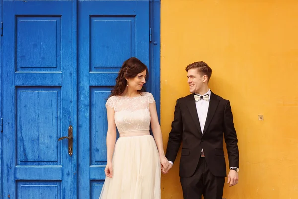 Bride and groom against yellow wall and blue door — Stock Photo, Image