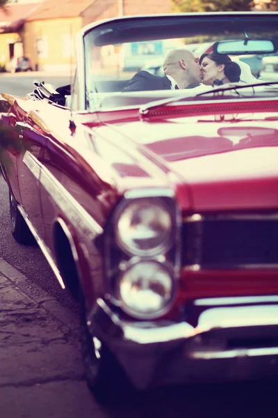 The bride and groom have fun behind the wheel of red retro vintage car.