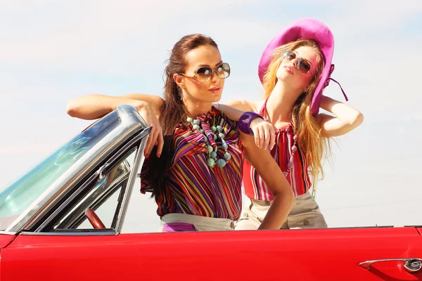 Красиві дами з сонцезахисними окулярами позує в старовинному ретро-автомобілі — стокове фото