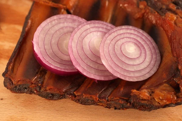 Schweinerippchen mit Scheiben roter Zwiebel auf einem Holzteller — Stockfoto