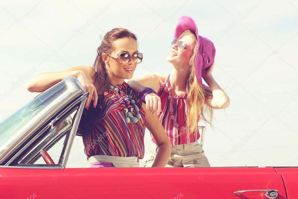 Beautiful ladies with sun glasses posing in a vintage retro car