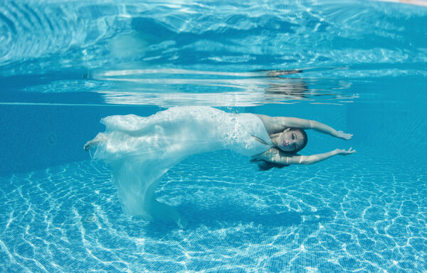 woman underwater swimming wearing her wedding dress
