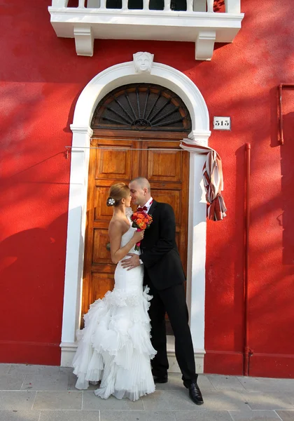 Groom and bride in front of a red house — Stock Photo, Image