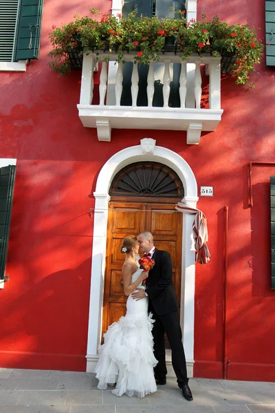 Novia y novio besándose delante de una casa roja — Foto de Stock