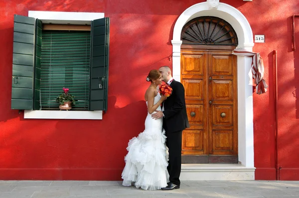 Sposa e sposo baciare accanto a una casa rossa — Foto Stock