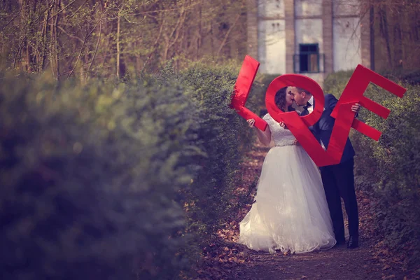 Bridal couple kissing holding big red love letters — Stock Photo, Image