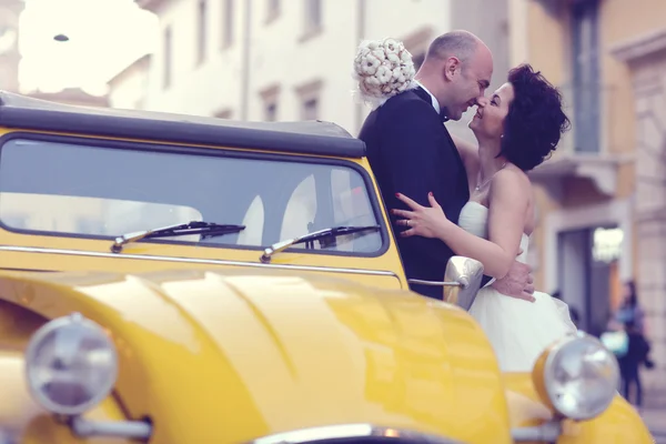Noiva e noivo beijando perto de carro amarelo — Fotografia de Stock