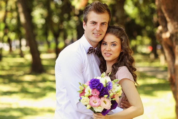 Bella coppia di sposi che si abbraccia nel parco e tiene bouquet — Foto Stock