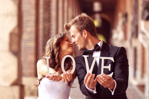 Beautiful bride and groom kissing and holding LOVE letters — Stock Photo, Image